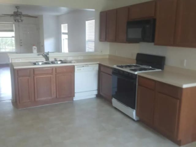 kitchen with a sink, a peninsula, white appliances, light countertops, and a ceiling fan