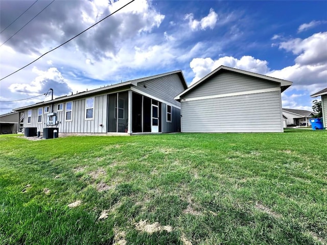 rear view of house with board and batten siding, a lawn, central AC, and a sunroom