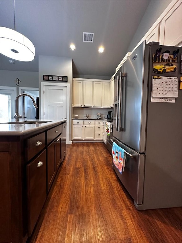 kitchen with visible vents, high quality fridge, dark brown cabinets, a sink, and dark wood-type flooring