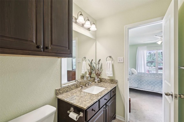 half bathroom featuring vanity, a textured wall, toilet, and ensuite bath