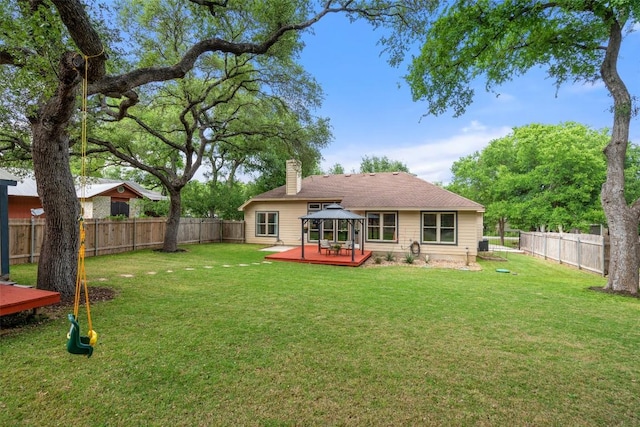 back of property with a chimney, a lawn, a wooden deck, a gazebo, and a fenced backyard