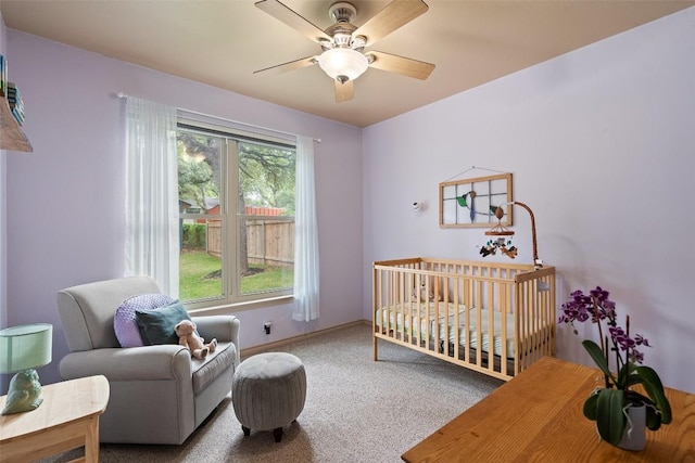 carpeted bedroom featuring a crib, baseboards, and a ceiling fan