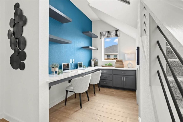 office space featuring baseboards, vaulted ceiling, light wood-type flooring, and built in desk