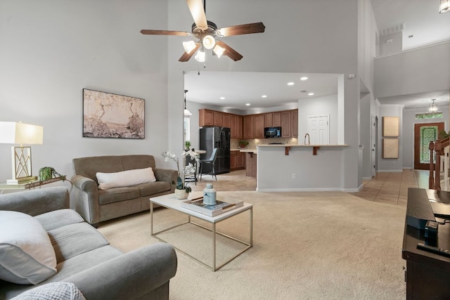 living room featuring ceiling fan, baseboards, a high ceiling, light carpet, and recessed lighting