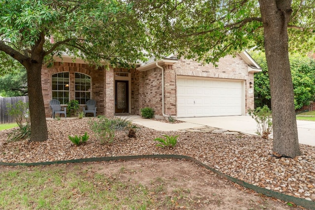 view of property hidden behind natural elements with brick siding, driveway, fence, and a garage