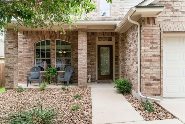 entrance to property featuring a porch, brick siding, and a garage