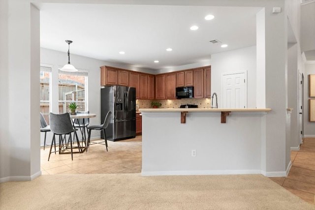kitchen featuring brown cabinets, a kitchen breakfast bar, recessed lighting, backsplash, and black appliances