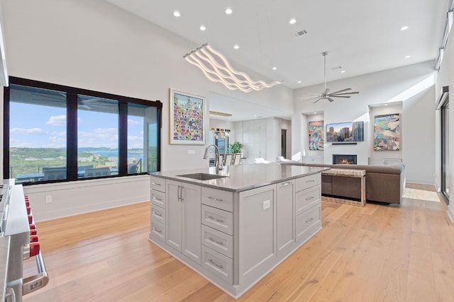 kitchen featuring ceiling fan, a sink, white cabinets, a warm lit fireplace, and light wood-style floors