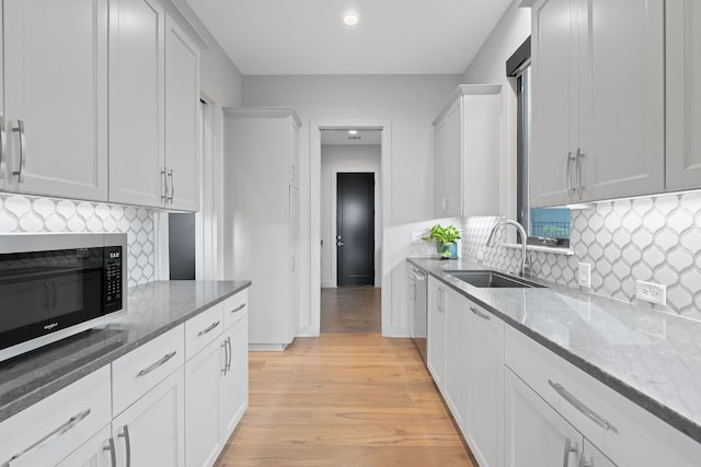kitchen with stainless steel dishwasher, light wood-style floors, light stone counters, a sink, and backsplash