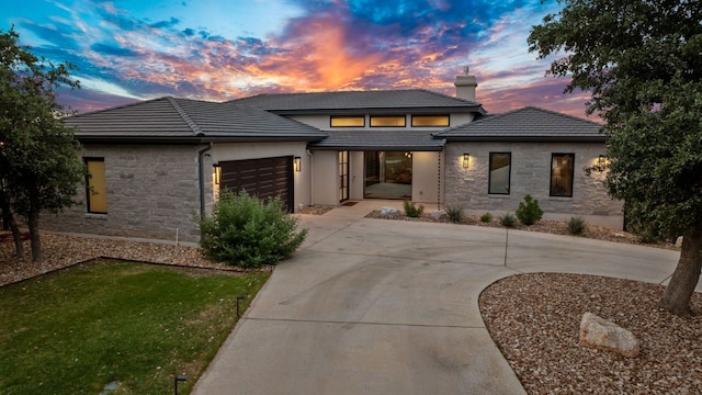 prairie-style house with concrete driveway, a tile roof, stone siding, and a garage