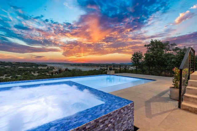 pool at dusk with a patio area, fence, and a pool with connected hot tub