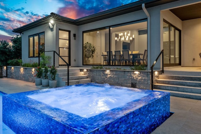 back of property with a patio, an in ground hot tub, and stucco siding
