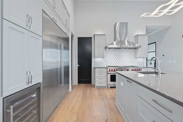 kitchen featuring wall chimney range hood, high end appliances, a sink, light wood finished floors, and wine cooler