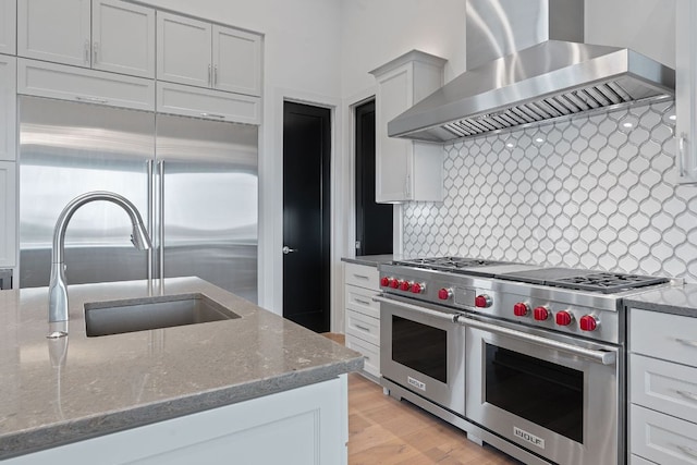 kitchen with decorative backsplash, stone counters, wall chimney range hood, and high quality appliances