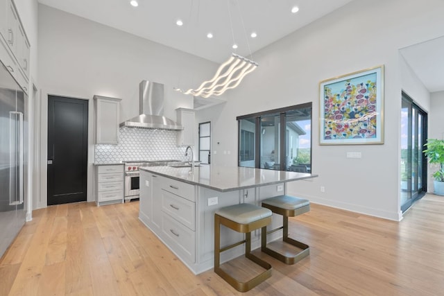 kitchen with high end appliances, wall chimney range hood, recessed lighting, light wood finished floors, and backsplash