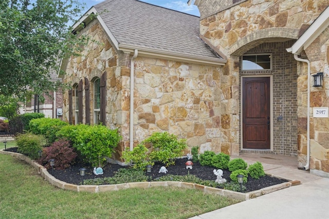 view of exterior entry featuring roof with shingles and stone siding