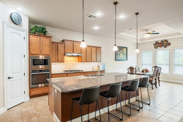 kitchen with brown cabinets, appliances with stainless steel finishes, a sink, baseboards, and tasteful backsplash