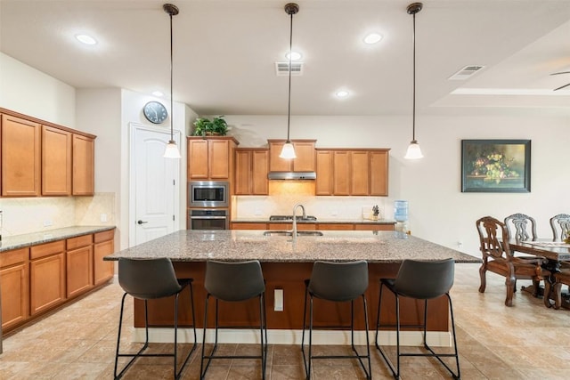 2917 Windy Vane Dr, Pflugerville, TX 78660 - kitchen featuring appliances with stainless steel finishes, under cabinet range hood, brown cabinets, backsplash, and recessed lighting