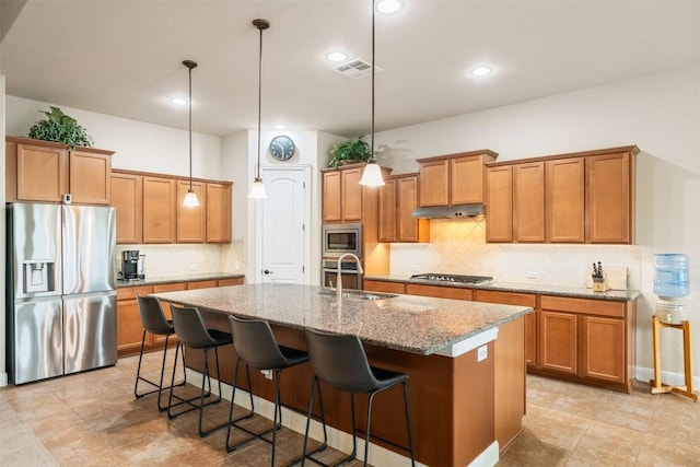 kitchen with brown cabinetry, visible vents, appliances with stainless steel finishes, a center island with sink, and a sink