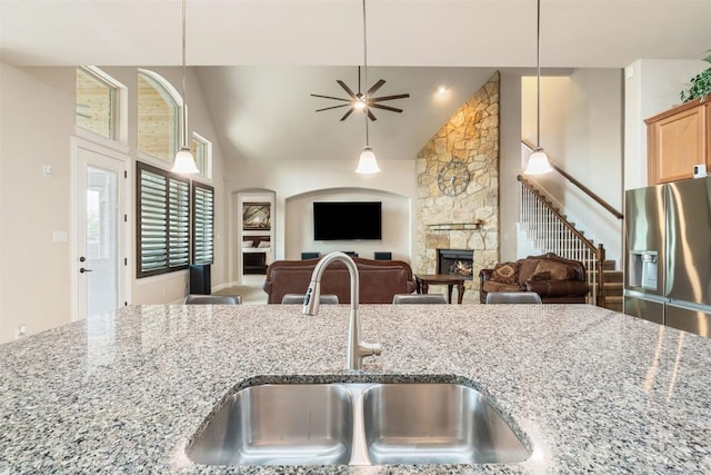 kitchen with a fireplace, a sink, stainless steel fridge with ice dispenser, high vaulted ceiling, and light stone counters