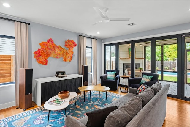living area with ceiling fan, light wood-style floors, a glass covered fireplace, recessed lighting, and visible vents
