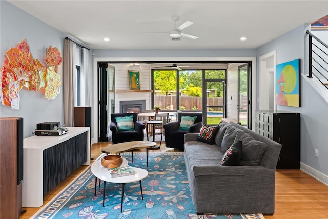 living room featuring recessed lighting, a ceiling fan, light wood-style flooring, and a glass covered fireplace