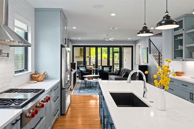 kitchen featuring appliances with stainless steel finishes, a sink, light countertops, open floor plan, and wall chimney exhaust hood