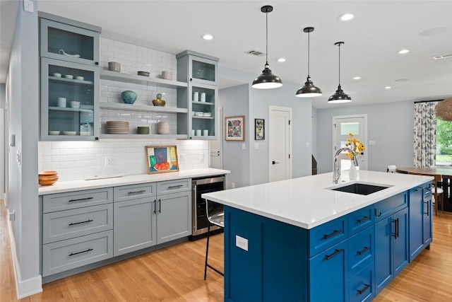 kitchen with visible vents, beverage cooler, light wood-style floors, tasteful backsplash, and a sink