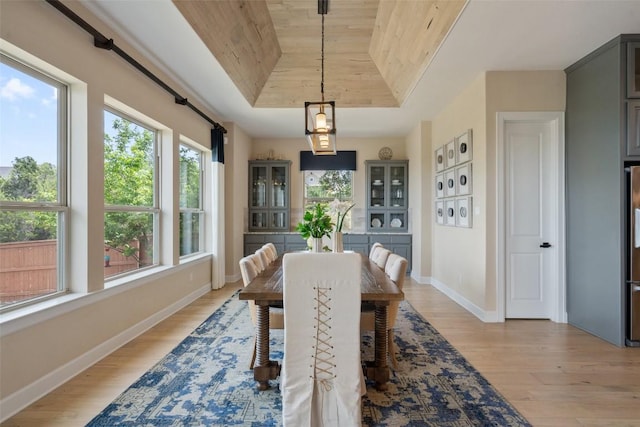 dining space with baseboards, light wood-style flooring, a raised ceiling, and wooden ceiling