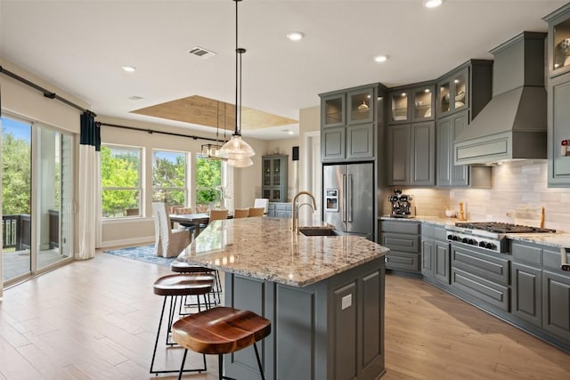 kitchen with visible vents, light wood-type flooring, a sink, premium range hood, and stainless steel appliances