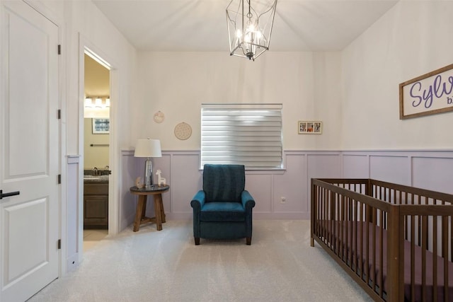 carpeted bedroom featuring connected bathroom, a notable chandelier, wainscoting, a sink, and a decorative wall