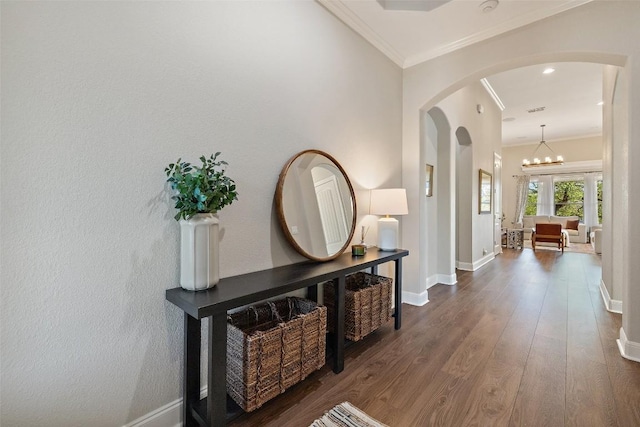 corridor featuring baseboards, arched walkways, wood finished floors, and ornamental molding