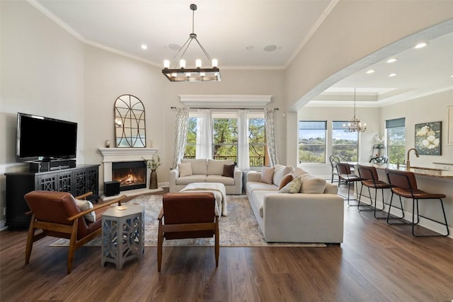 living area with crown molding, a warm lit fireplace, a notable chandelier, and dark wood finished floors
