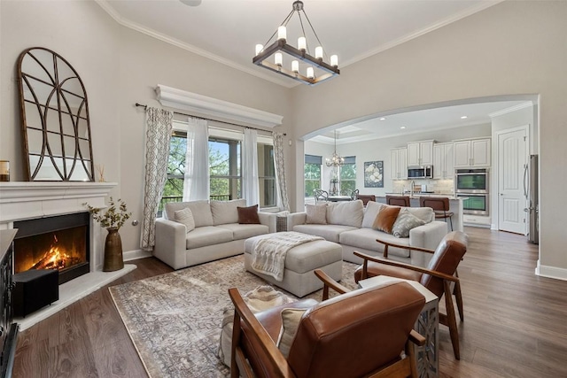 living area featuring ornamental molding, arched walkways, wood finished floors, and a chandelier