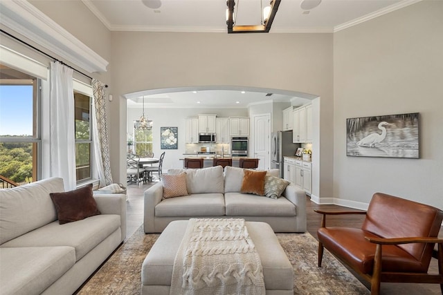 living room featuring crown molding, arched walkways, wood finished floors, and a chandelier
