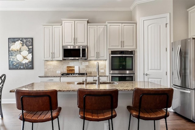 kitchen featuring appliances with stainless steel finishes, a sink, a kitchen bar, backsplash, and dark wood-type flooring