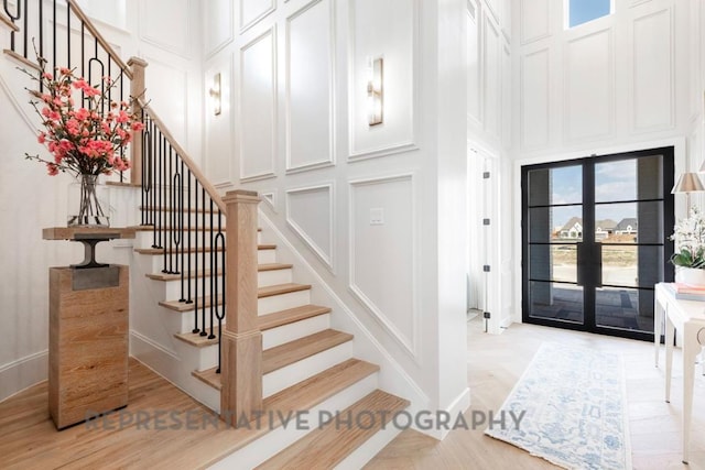 foyer with a high ceiling, light wood-type flooring, stairway, and a decorative wall