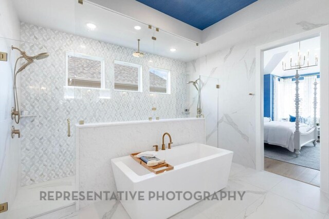 full bath with connected bathroom, a walk in shower, an inviting chandelier, plenty of natural light, and marble finish floor