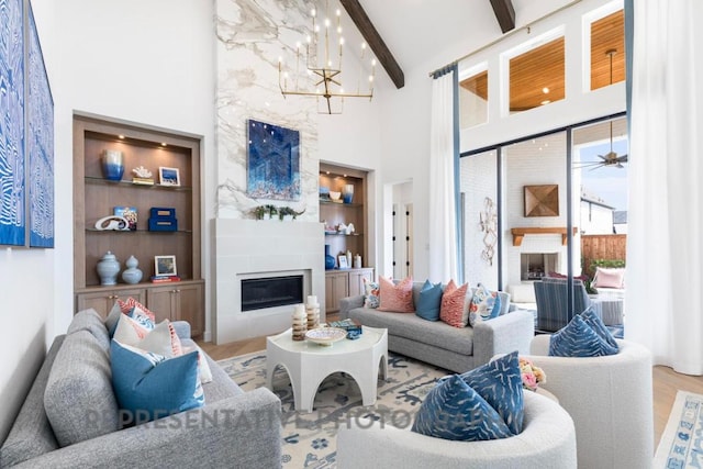 living area featuring a towering ceiling, wood finished floors, beamed ceiling, built in shelves, and a large fireplace
