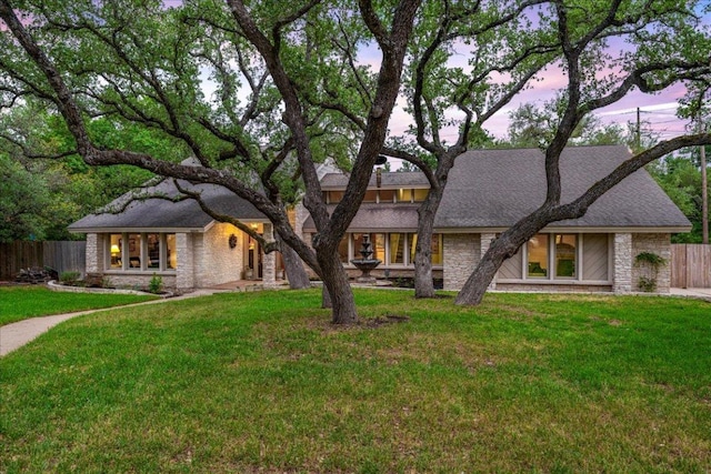 view of front of property with roof with shingles, fence, stone siding, and a front yard