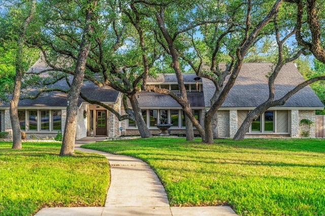 view of front of property featuring stone siding, a front yard, and roof with shingles