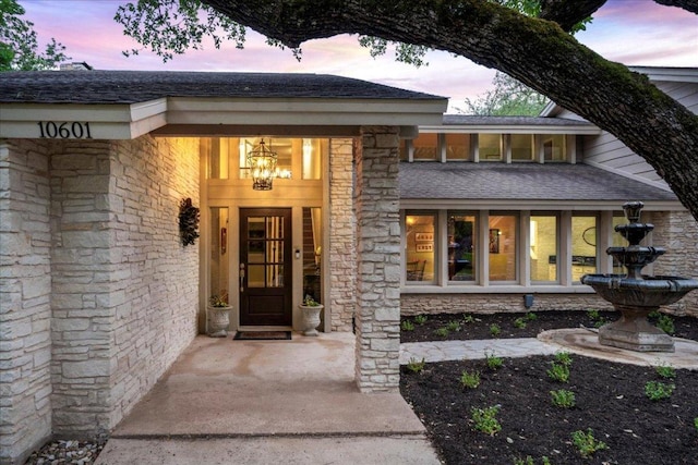 doorway to property featuring a shingled roof and stone siding