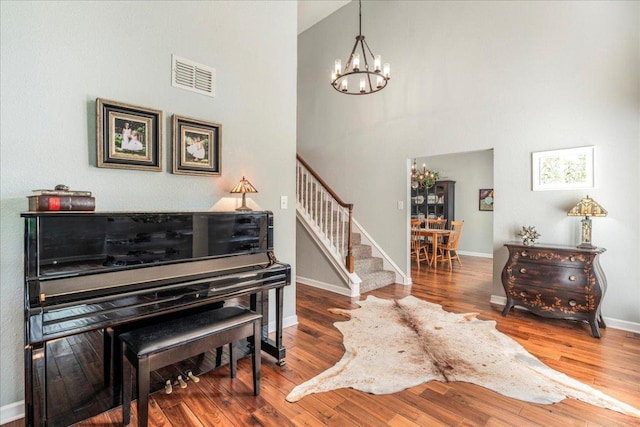living area with visible vents, stairway, baseboards, an inviting chandelier, and a high ceiling