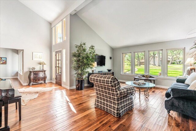 living room featuring high vaulted ceiling, baseboards, and wood finished floors