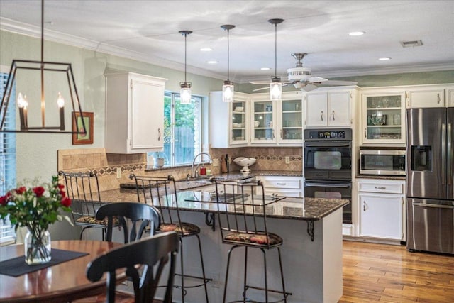 kitchen with visible vents, a peninsula, glass insert cabinets, a sink, and black appliances