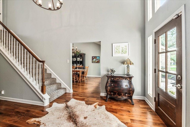 entrance foyer featuring stairs, baseboards, an inviting chandelier, and wood finished floors
