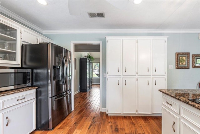 kitchen featuring appliances with stainless steel finishes, dark stone countertops, white cabinetry, visible vents, and hardwood / wood-style flooring