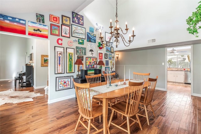 dining room with a notable chandelier, high vaulted ceiling, baseboards, wood finished floors, and visible vents