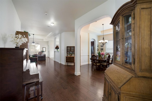 foyer featuring arched walkways, baseboards, a raised ceiling, and dark wood-type flooring