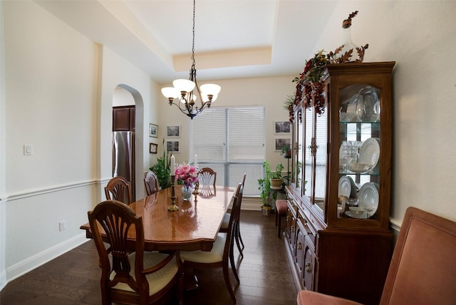 dining space featuring baseboards, a chandelier, a tray ceiling, arched walkways, and dark wood finished floors